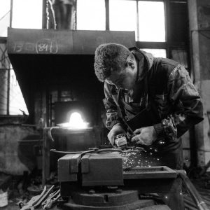 Blacksmith using a grinder in a workshop, creating sparks.