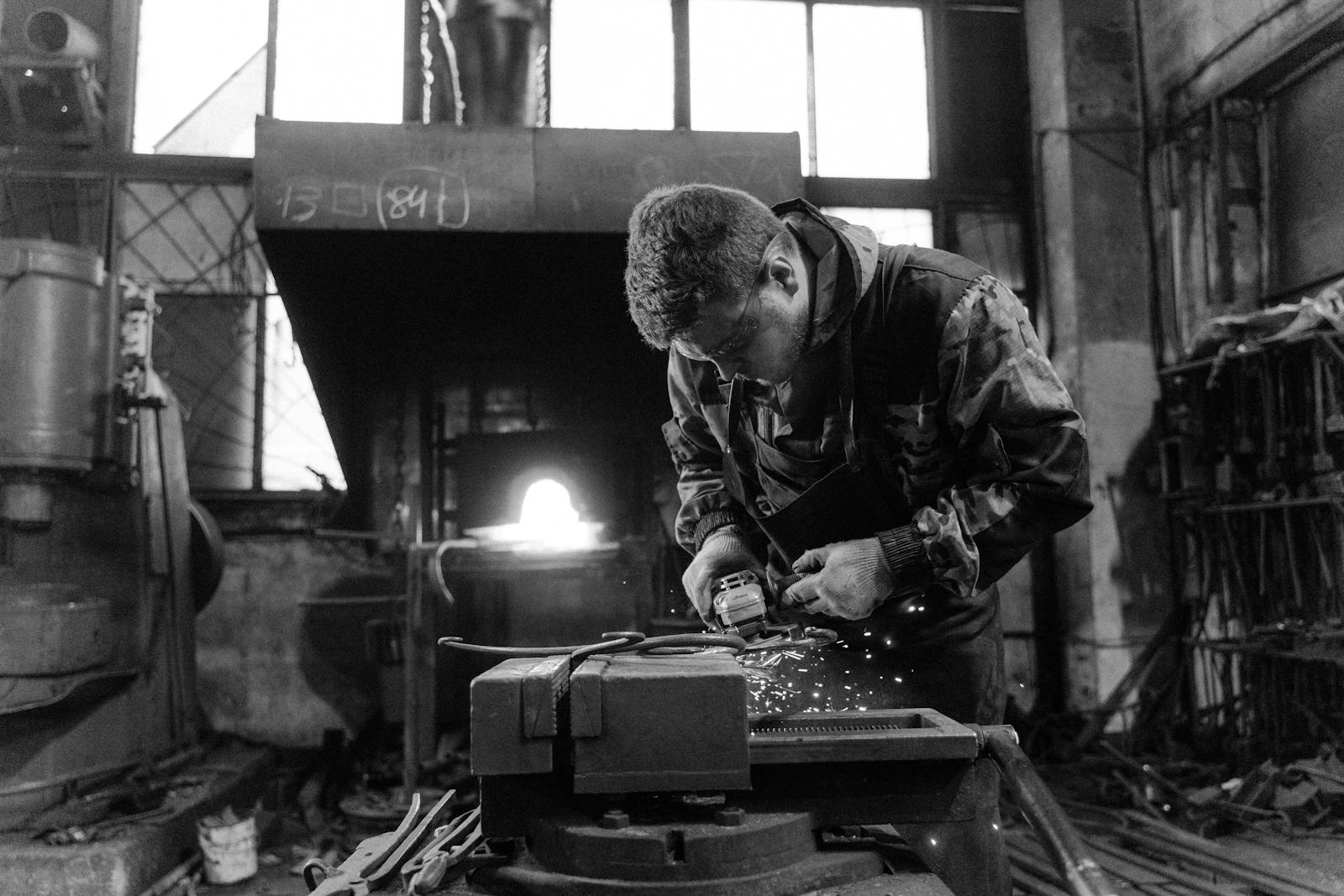 Photo by Tima Miroshnichenko Blacksmith using a grinder in a workshop, creating sparks.
