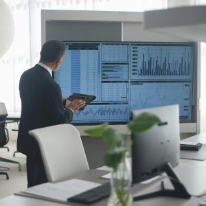 Professional in suit analyzing financial data on screens in a modern office setting.