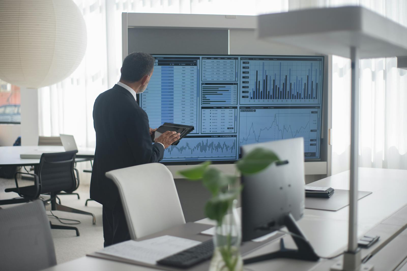 Photo by Kampus Production Professional in suit analyzing financial data on screens in a modern office setting.